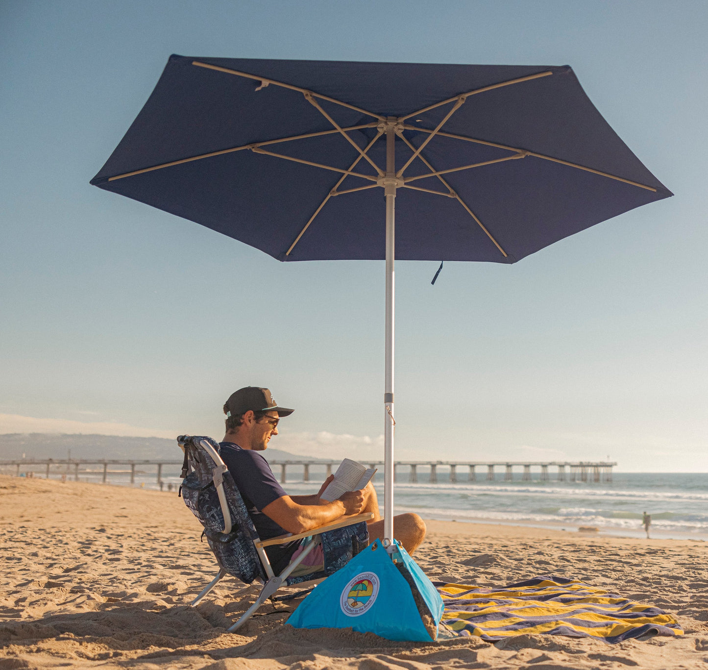 man reading a book at the beach underneath a beachBUB umbrella