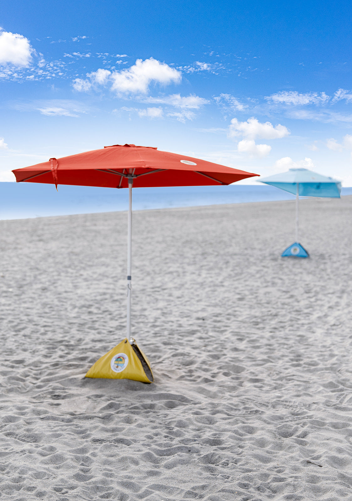 two wind resistant beach umbrellas set up on the shore of a beach