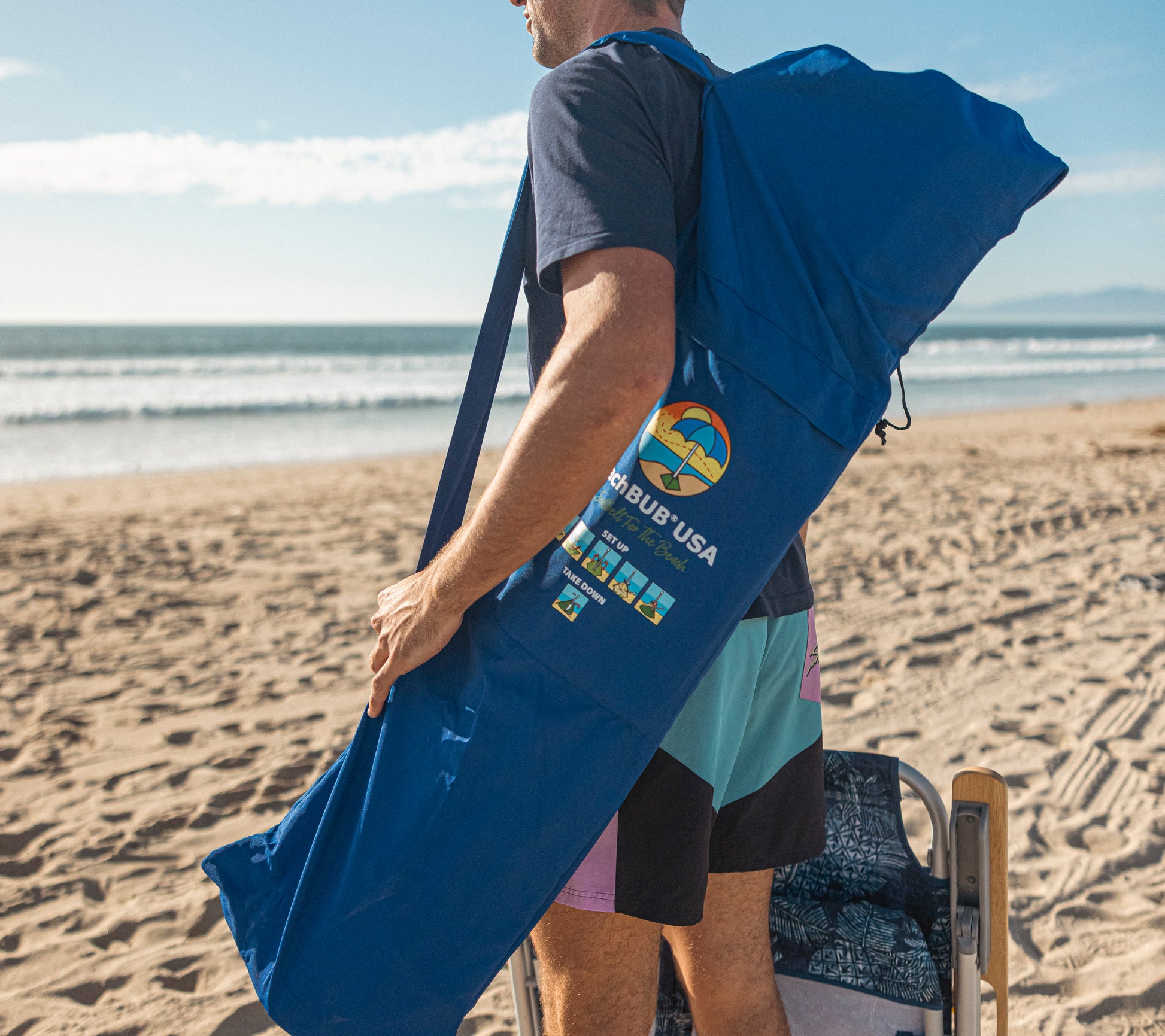 man walking along beach with beach umbrella bag